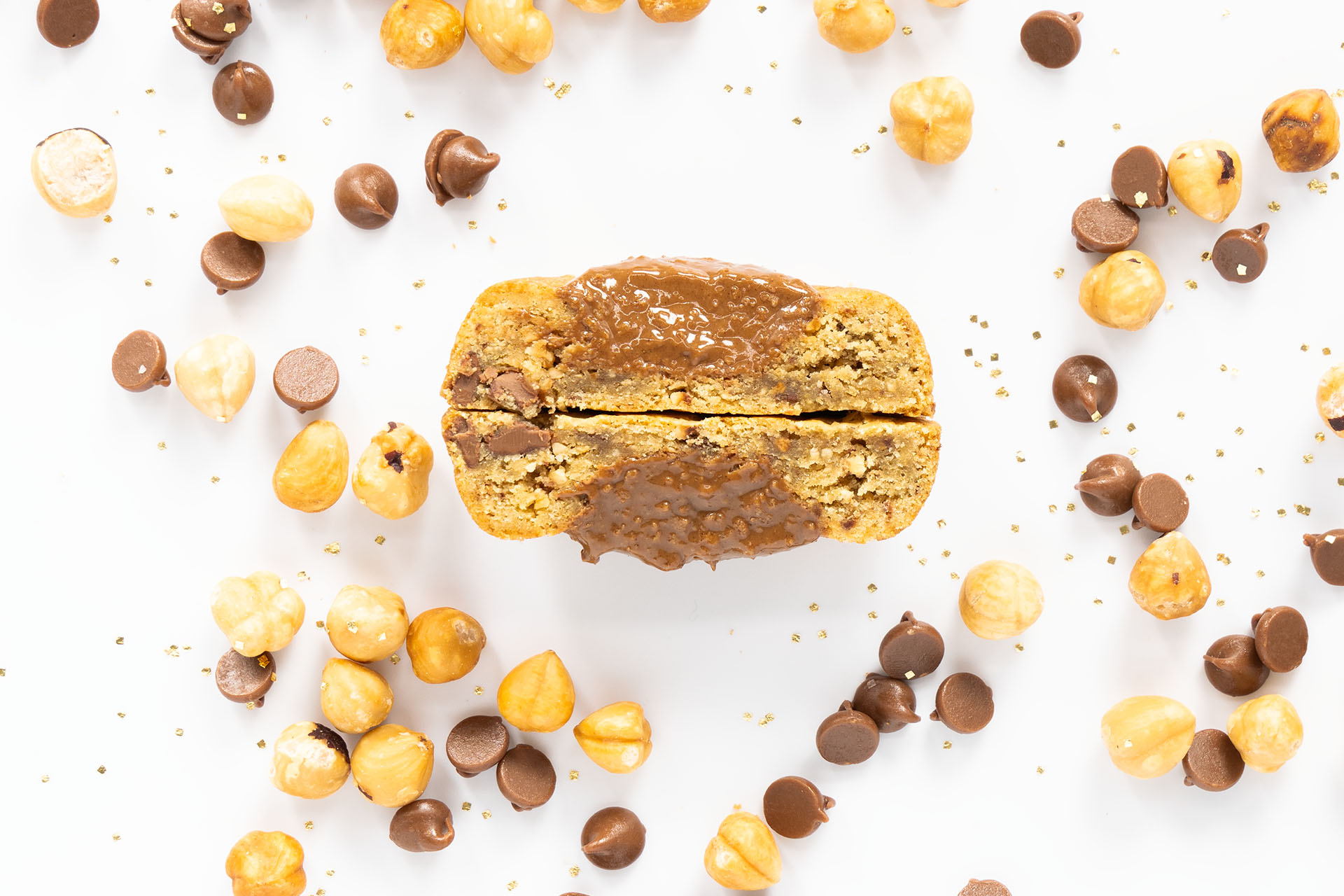 Sliced loaf of bread with caramel drizzle and espresso surrounded by nuts and chocolate chips on a white background.