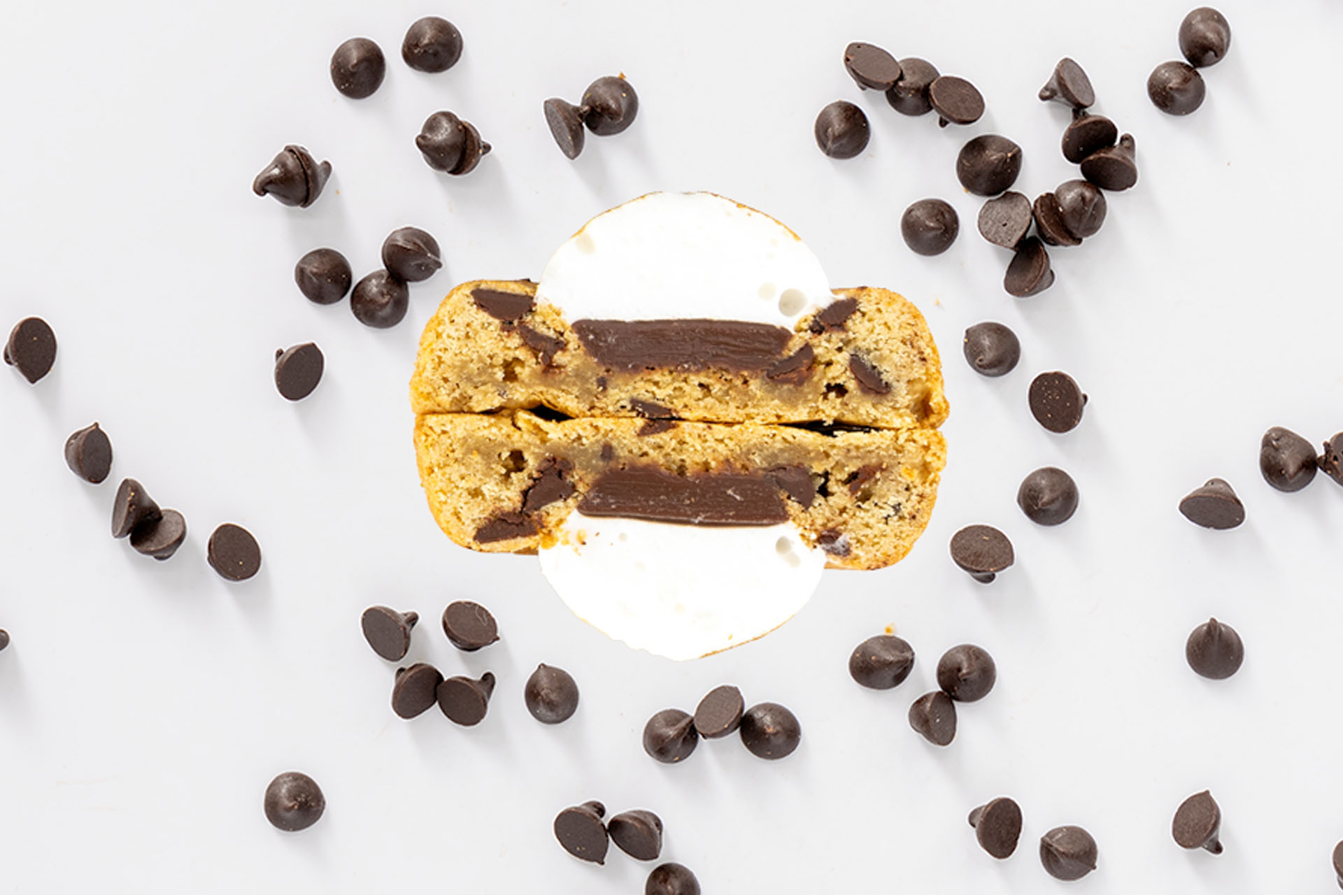 A chocolate chip cookie and espresso ice cream sandwich cut in half, surrounded by scattered chocolate chips on a white surface.