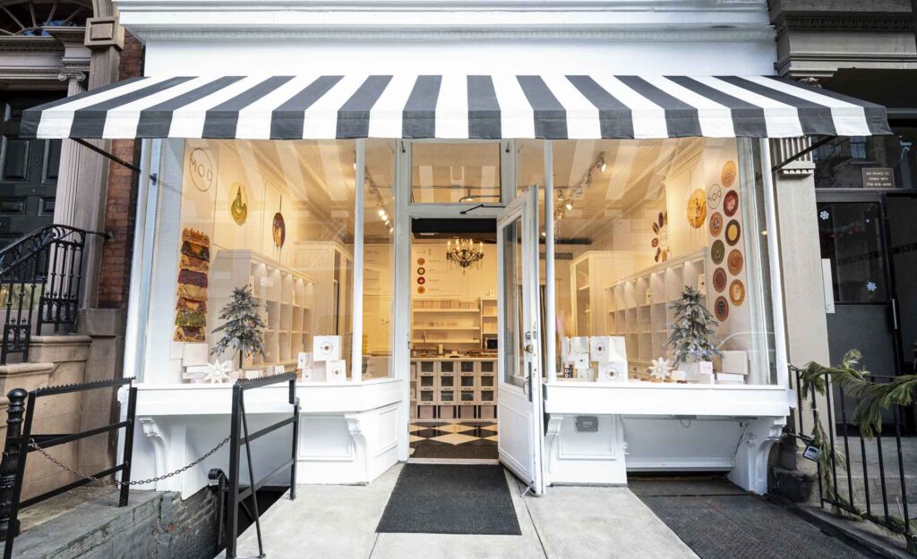 A small, well-lit boutique shop with a black and white striped awning, displaying products in its window and a checkered floor visible inside, featured prominently on "Homepage 001" for its