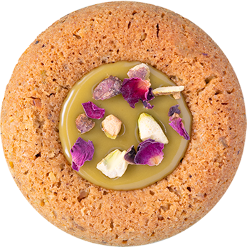 A single round cracker topped with a dollop of green spread and garnished with edible flower petals.
