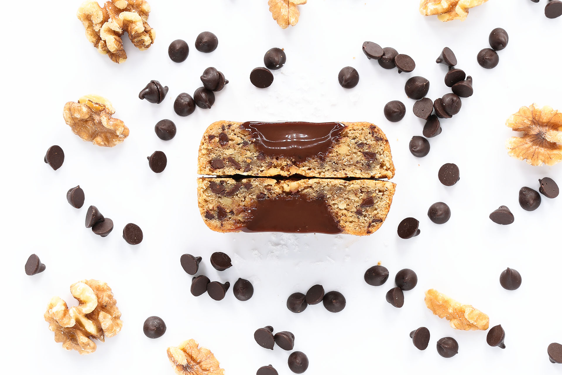 Chocolate-drizzled blondie surrounded by walnuts and chocolate chips on a white surface, with a hint of espresso.