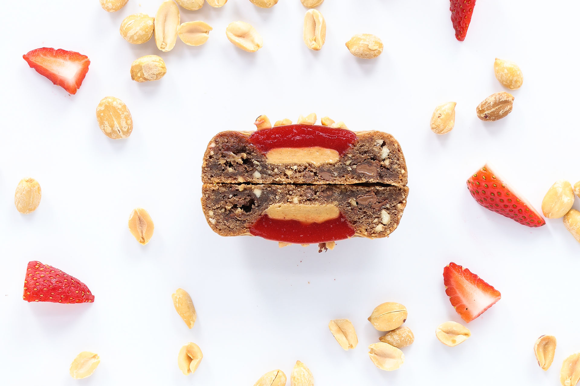 A cross-section of a layered dessert bar with a peanut and espresso strawberry topping on a white surface.