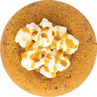 Round cookie topped with popcorn and drizzled with caramel sauce on a white background.