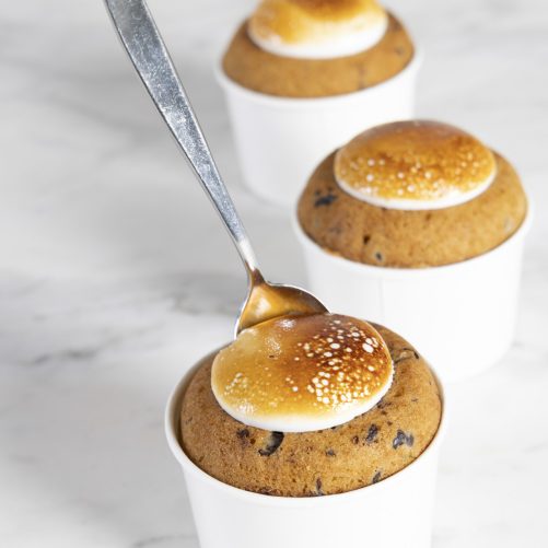 Three chocolate chip muffins in white cups with a spoon drizzling caramel on top, perfect for the homepage.