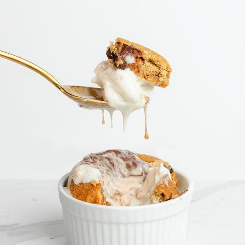 A spoon holds a dripping portion of a dessert topped with melted ice cream, hovering above a white ramekin containing more of the same treat. This tempting scene is like something you'd find on the homepage of your favorite dessert blog.